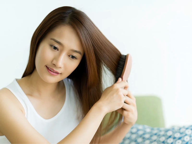 タンクトップを着て部屋で髪の毛をブラッシングしている女性