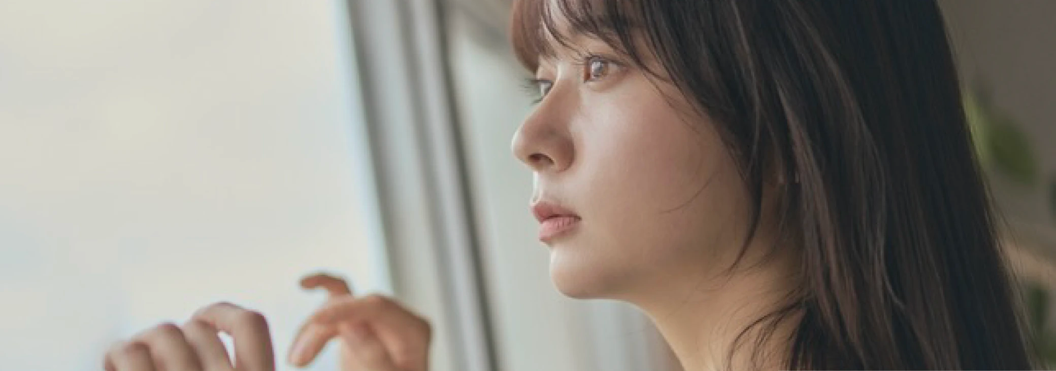 グレージュの髪色をして窓の外を眺めている女性