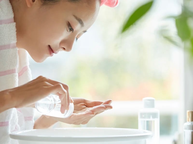 頭にタオルを巻き、洗面台で肌や髪のケアをする女性