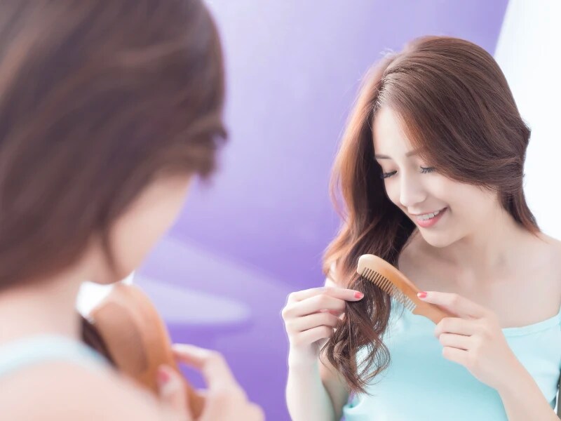 鏡の前でコームで毛先をとかしながら微笑んでいる女性