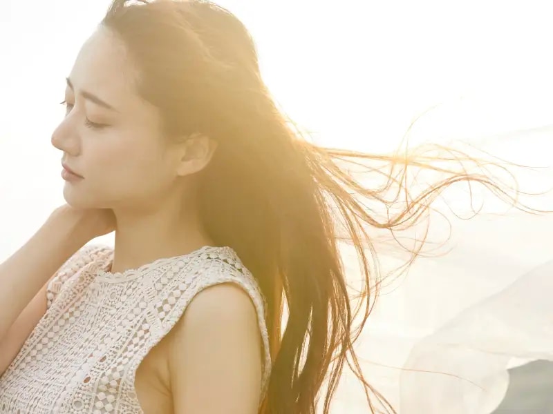 風に髪をなびかせて目を閉じている女性