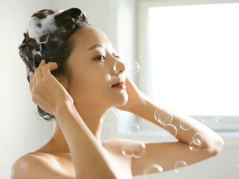 バスルームでシャンプーで髪を洗っている女性