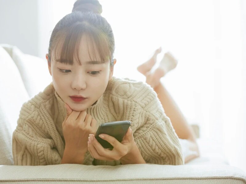 ソファーにうつ伏せになりながらスマホの画面を見ている女性