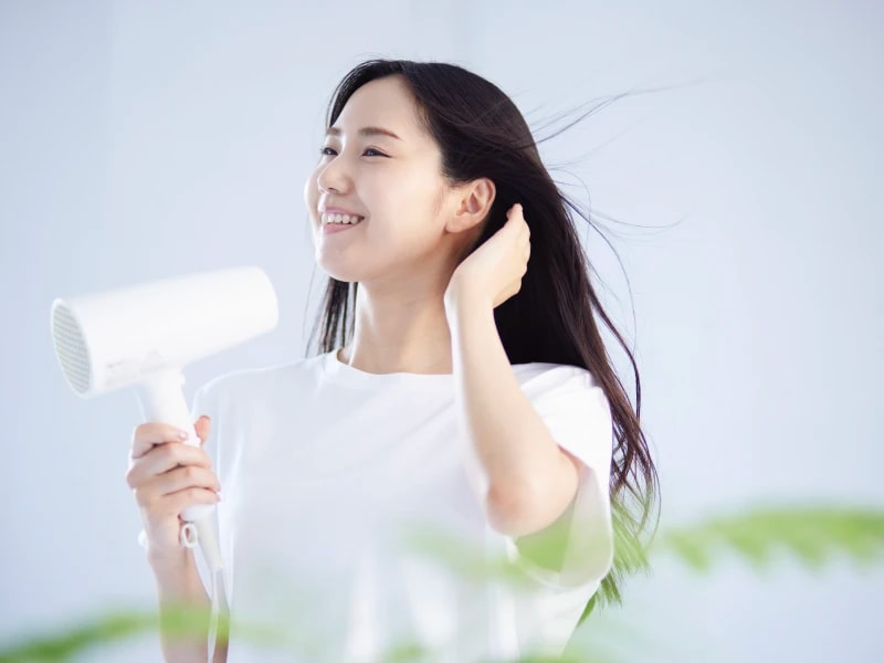 部屋で髪に白いドライヤーで風を当てている女性