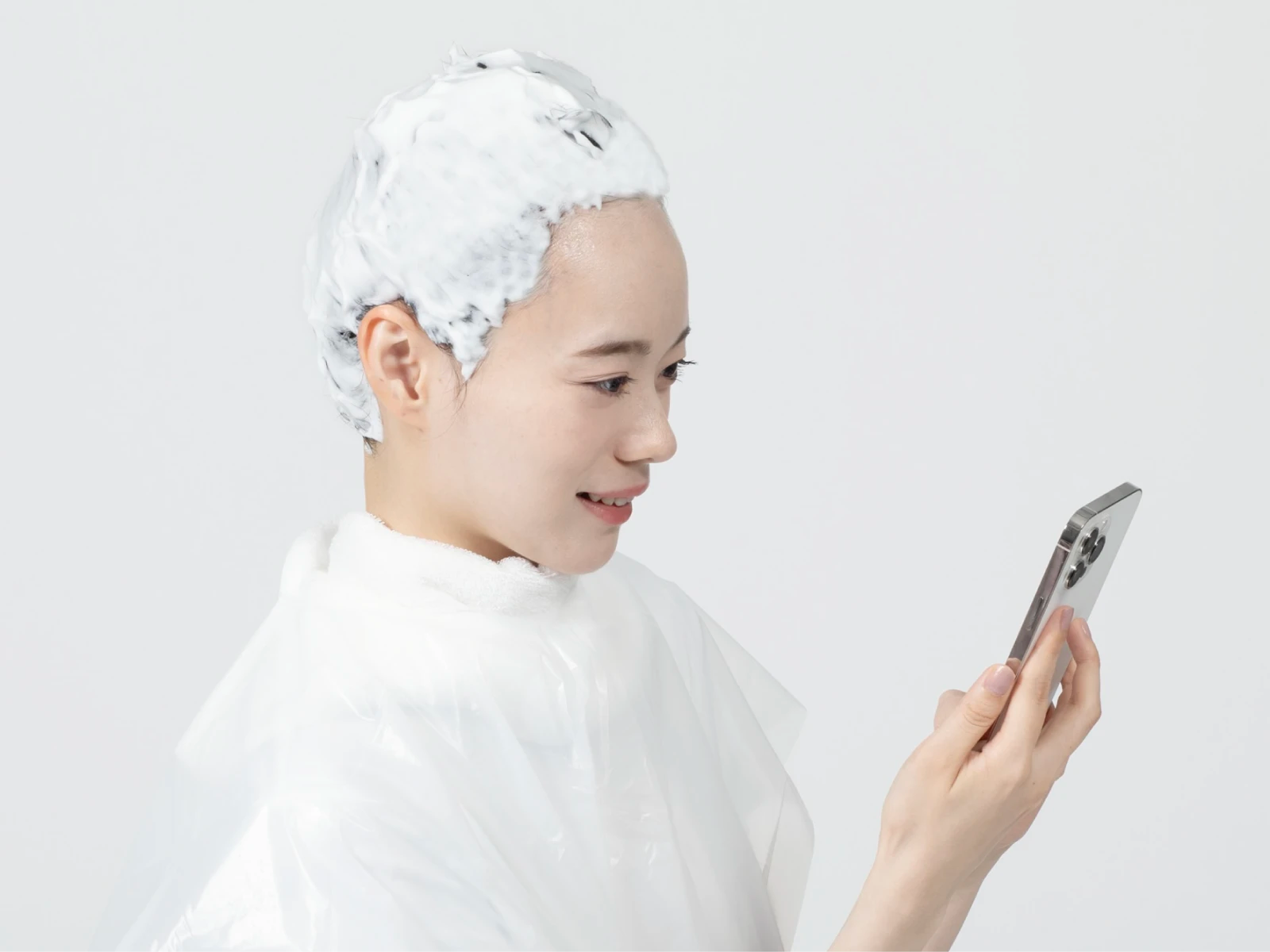 ケープを巻いてビューティラボを髪全体に塗布した状態でスマホを見ている女性