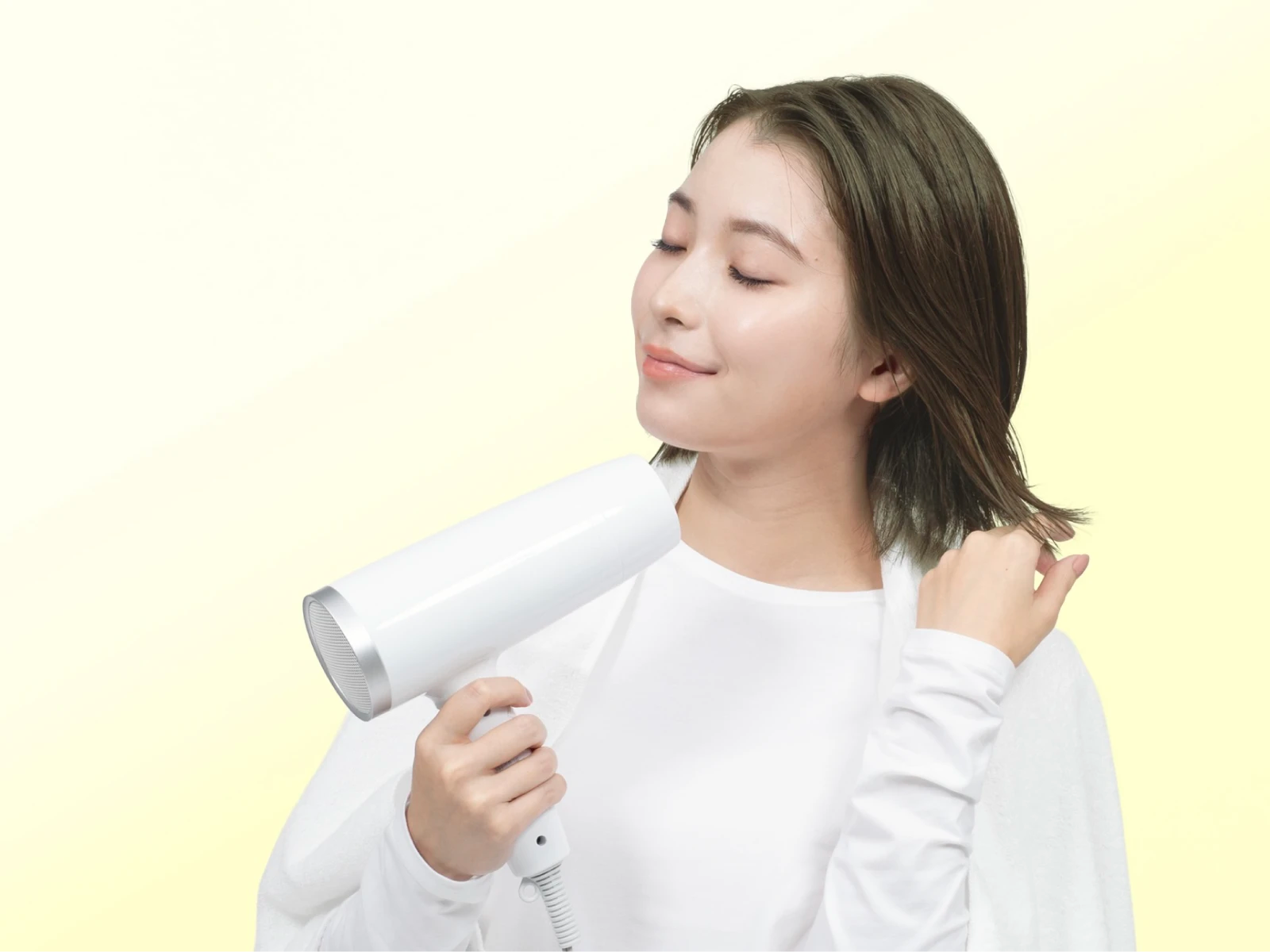 ビューティラボ/ピスタチオアッシュの髪色をして微笑みながら髪にドライヤーをかけている女性