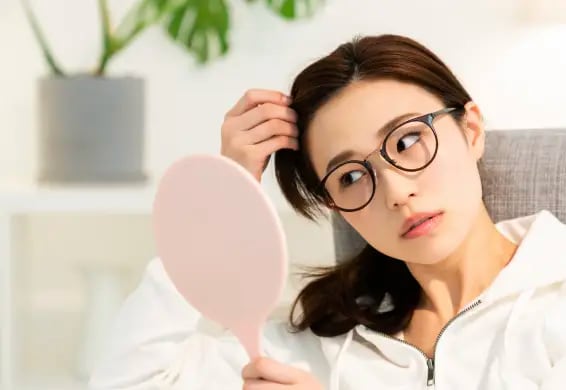 髪を触りながら手鏡に写った自分を見つめている眼鏡をかけた女性